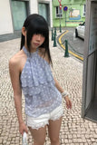 Woman in a light blue polka dot top and white shorts standing on a street.