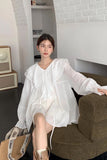 Woman in a white dress sitting on a brown chair in a room with white walls.