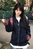 A young woman wearing a dark blue denim jacket with red and black plaid lining on the cuffs, layered over a white t-shirt and paired with a matching plaid backpack, standing outdoors.