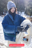 Person in winter clothing holding a white blanket with a child illustration in a snowy landscape.