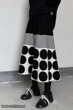 Person wearing a black and white polka dot skirt with a plain background