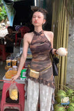 Woman holding a coconut in an outdoor setting with a child and various items in the background.