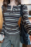Person wearing a striped shirt with a black bag and a drink, standing indoors.