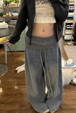 Person wearing a black jacket, white crop top with text, and gray wide-leg pants in an indoor setting.