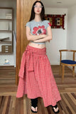 Person wearing a gray crop top with a red flower design and a red checkered skirt in a room.
