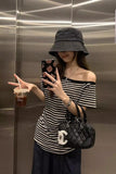 A woman takes a mirror selfie in an elevator wearing a black and white striped off-the-shoulder top, a dark gray bucket hat, and a black quilted Chanel shoulder bag with a white CC logo.