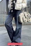 Person wearing a white puffer jacket, dark blue jeans, and holding a beige handbag on a city street.