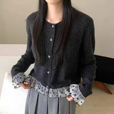 Person wearing a dark gray cardigan with checkered cuffs and hem, standing against a neutral background.