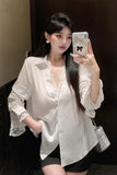 Woman taking a mirror selfie wearing a white blouse and black shorts.