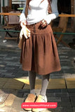 Person wearing a brown skirt and white top outdoors with a visible brand watermark.