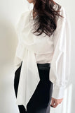 Person wearing a white layered shirt over a black outfit against a plain background