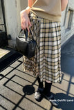 Person wearing a plaid skirt and holding a black handbag on a street.