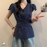 Person wearing a blue checkered top and light gray pants against a plain background
