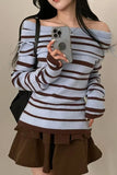 Person wearing a striped sweater and brown skirt holding a phone.
