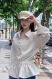 Woman wearing a white striped shirt and beige cap on a city street.