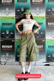 Woman posing in front of Expnst Fleet posters wearing a white crop top and green plaid shorts.
