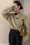 Person wearing a beige knitted sweater with a high collar, holding a brown bag against a plain background.