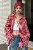 Person wearing a red checkered shirt, white top, blue jeans, and a red cap indoors.