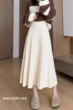 Person wearing a brown sweater, white skirt, and beige shoes indoors.