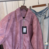 Pink jacket with a tag on a hanger next to blue jeans.