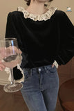 Person wearing a black top with lace collar and blue jeans, holding a glass.