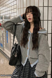 Woman wearing a gray cardigan and plaid skirt with headphones, standing against a tiled wall.
