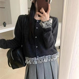 Person wearing a dark gray cardigan with checkered details, holding a phone, and carrying a black bag.
