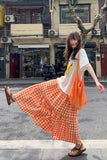 Woman in an orange and white checkered skirt and white top standing on a street.
