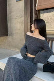 Woman wearing a dark gray off-shoulder top and skirt sitting on a wooden floor.