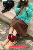 Person wearing a teal sweater and brown skirt sitting on a sidewalk with a black dog lying nearby.
