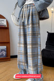 Person wearing blue plaid pants in a room with a bookshelf and lamp.