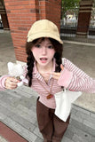 Person wearing a beige cap and striped shirt, holding a plush toy and white bag, standing on a sidewalk.