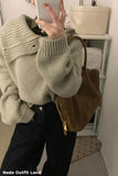 Person wearing a light green sweater and holding a phone, with a brown bag over their shoulder.