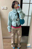 Person wearing a light blue knitted cardigan and floral pants, taking a mirror selfie.