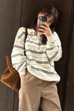 Person taking a mirror selfie wearing a striped shirt and beige pants against a brown wall.
