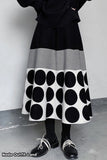 Person wearing a black and white polka dot skirt with a plain background
