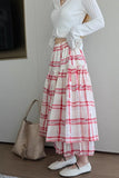 Person wearing a white long-sleeve top and red plaid skirt with a woven handbag indoors.