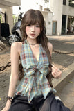 Woman wearing a plaid top with a large bow sitting on a street.