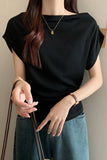 A woman wearing a black short-sleeve top with a wide boat neckline, paired with blue jeans and gold jewelry, holding a brown strap.