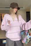 Person wearing a pink sweater and brown cap, holding a colorful bag indoors.