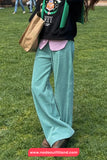 Person wearing a black sweatshirt with a logo, teal pants, and brown shoes on grass.