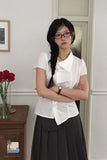 Woman wearing glasses and a white blouse with a black skirt in an indoor setting.