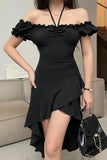 A woman wearing a black off-the-shoulder mini dress with ruffled sleeves, a gathered sweetheart neckline, ruched bodice, and an asymmetrical layered ruffle hem. She is holding a black handbag with a gold chain strap in an indoor setting.
