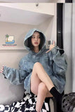 Person wearing a denim hoodie sitting on a chair with a visible brand logo in the corner.