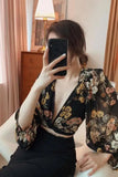 Person wearing a floral kimono-style garment in a room with curtains and a dresser.
