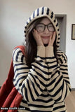 Person wearing a striped sweater with a hood in a room.