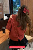 Person wearing a red cardigan with a large bow in a cafe setting, with a visible brand watermark.