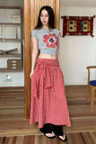 Woman wearing a gray t-shirt with a floral design and a red checkered skirt in a room.