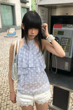 Woman in a polka dot top and white shorts standing next to a payphone.