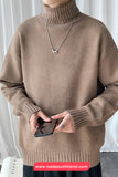 Person wearing a brown turtleneck sweater holding a phone, with a white curtain background.
